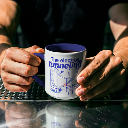 Person holding a white mug with blue inside 'The electron tunneling' design on a reflective surface.