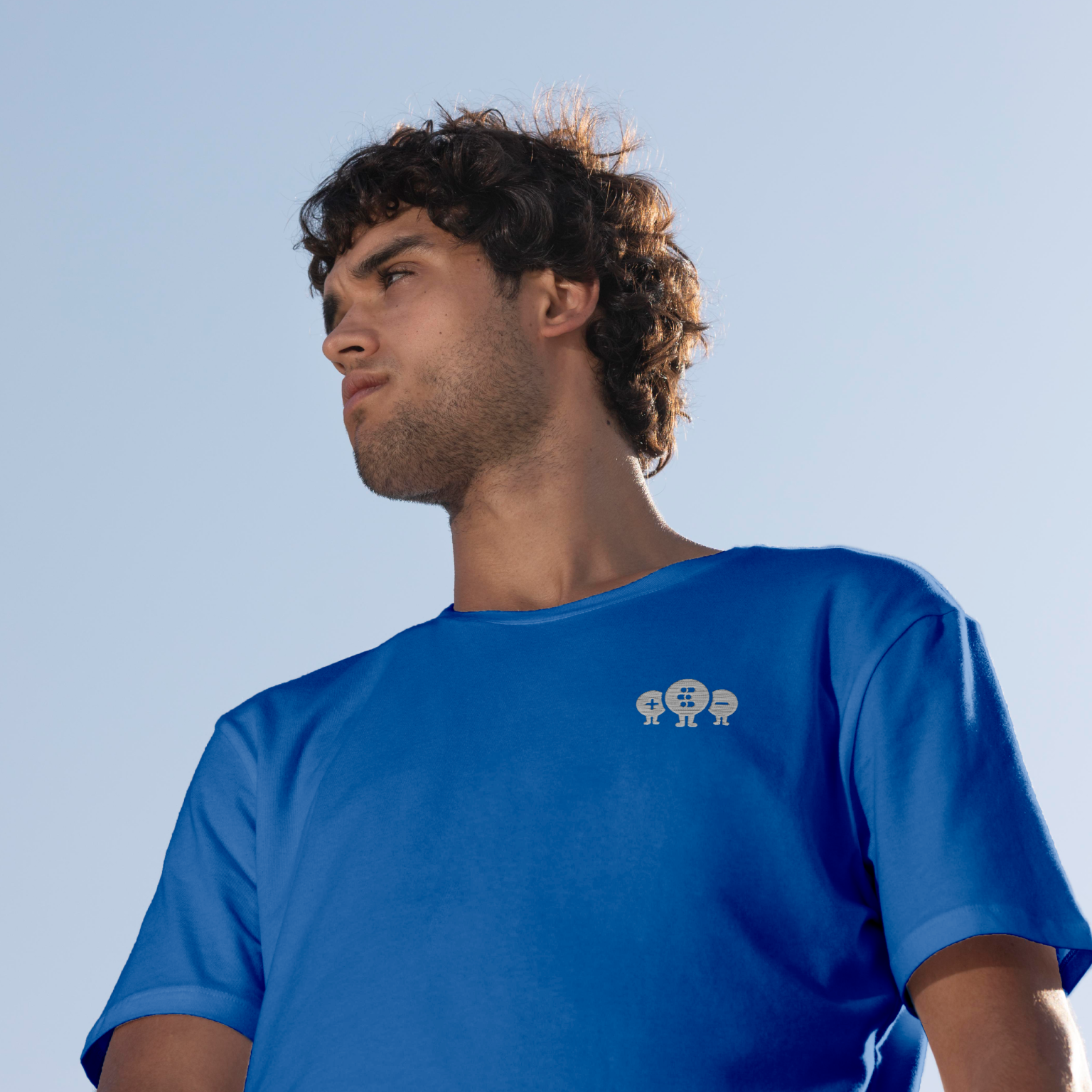 Man wearing a blue t-shirt with quantum tryon embrodery on a blue background, angle from bottom to top